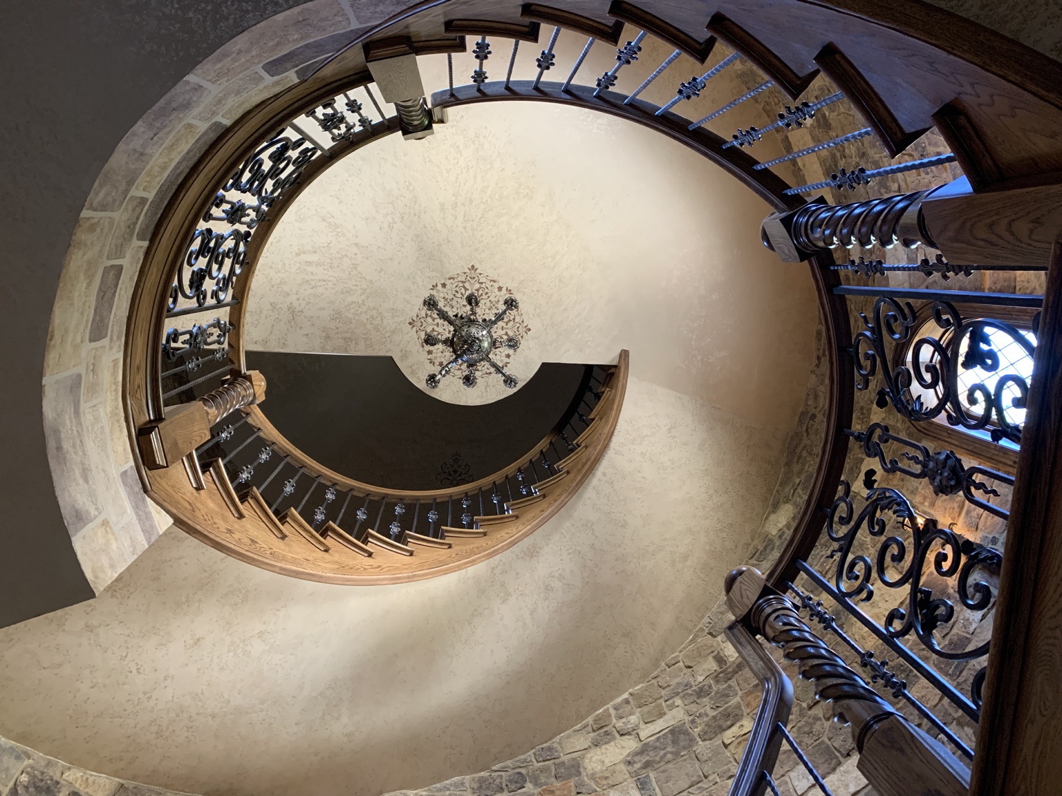 Upward view through a circular custom staircase with wood railings and ornamental ironwork.