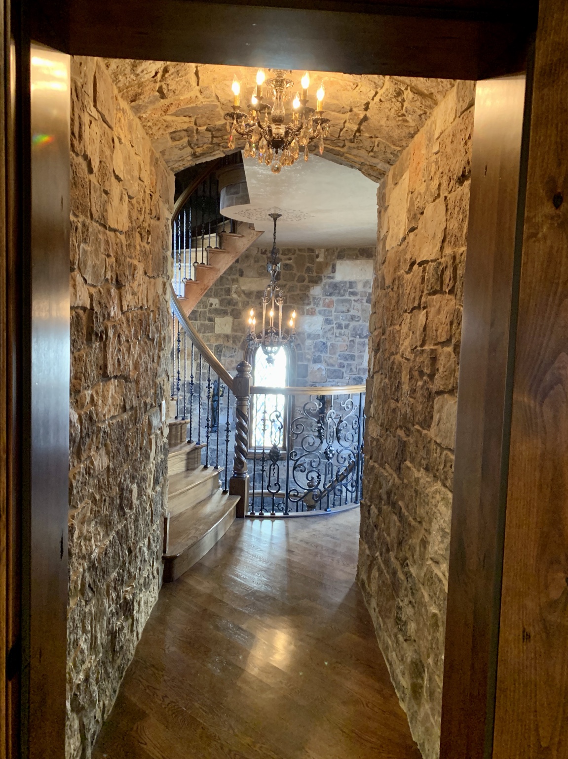Stone-lined passage opening to a curved custom staircase in a European-inspired Naperville home.