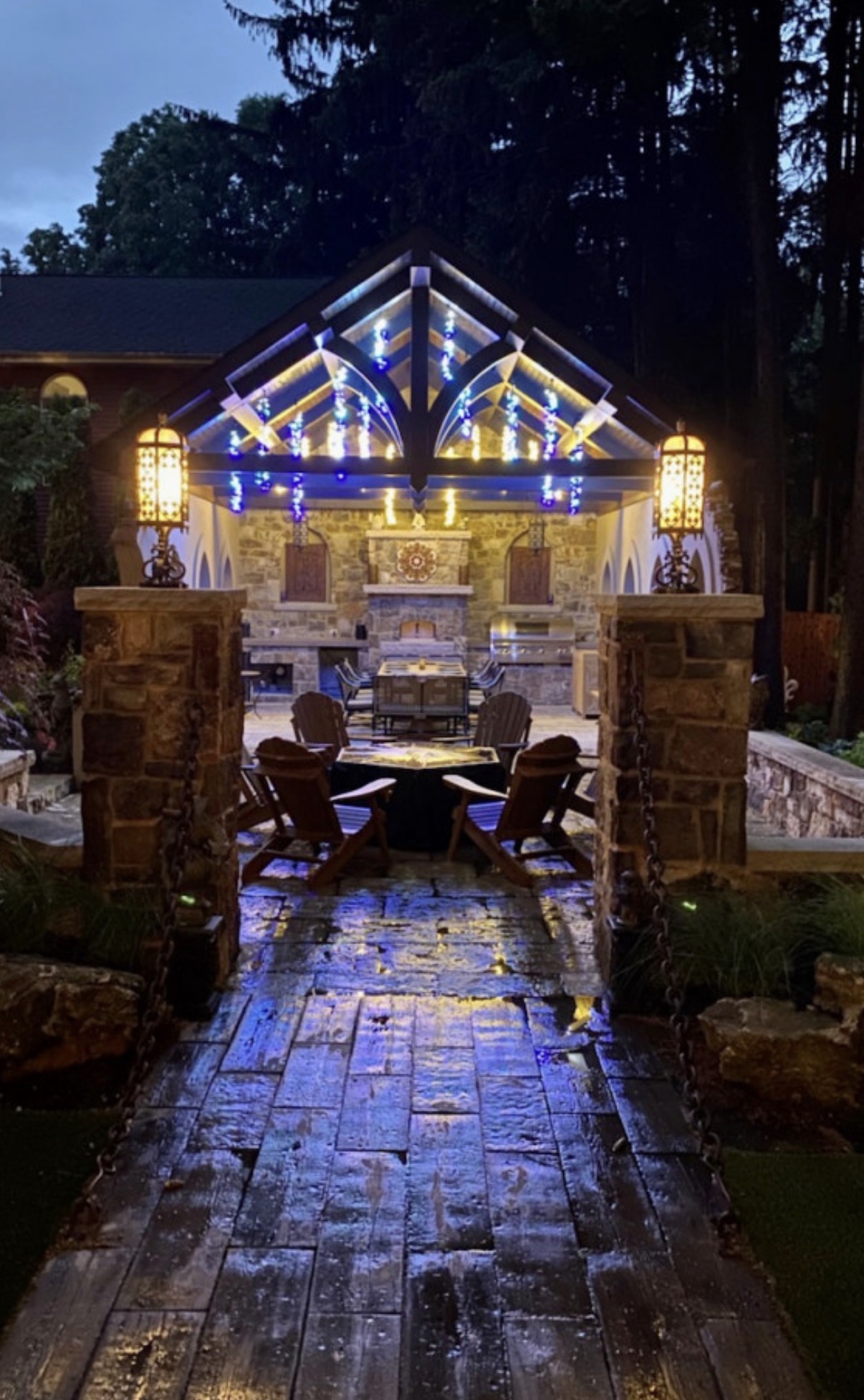 Illuminated outdoor pavilion at dusk with stone columns and wet stone paving.